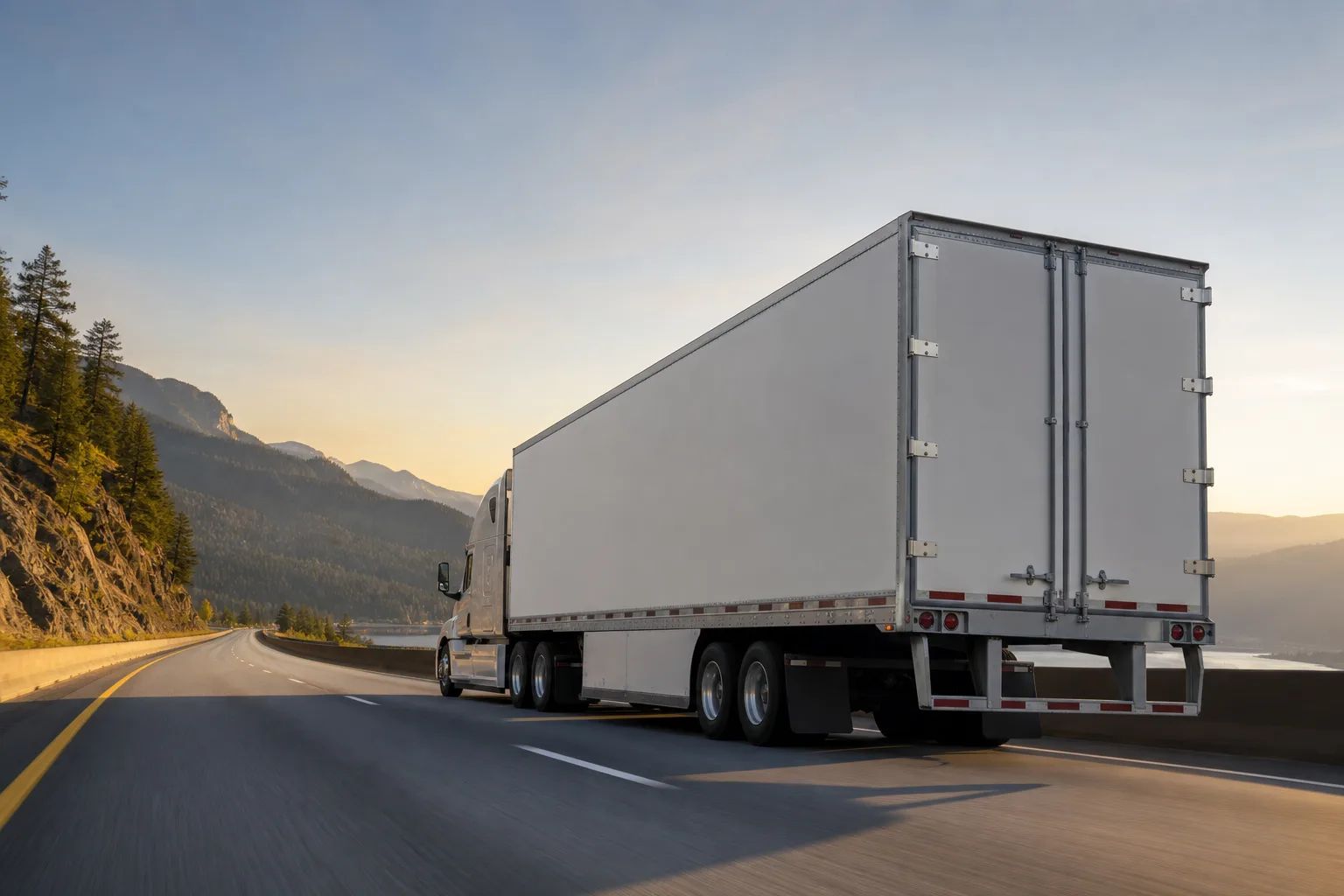 An unbranded long-haul freight truck travels a mountain highway at golden hour.
